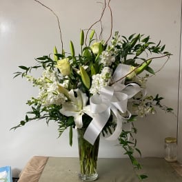 White lilies and roses in a tall glass vase with a white ribbon