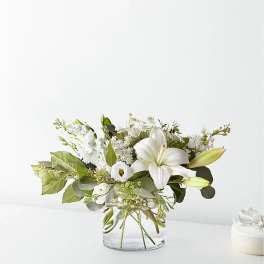White lilies and small white blooms arranged in a clear glass vase