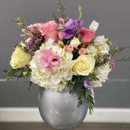 Mixed pink, white, and purple flowers arranged in a silver vase