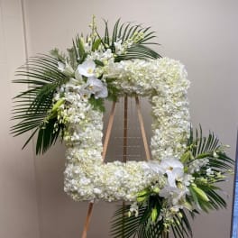 Large white floral wreath on an easel with palm fronds and orchids