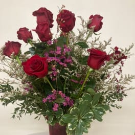 Red roses arranged in a tall burgundy vase with pink filler flowers