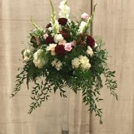 Tall floral arrangement in a clear vase with burgundy, pink, and white blooms