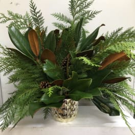 Green holiday arrangement in a gold textured vase with pinecones