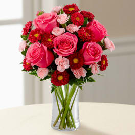 Pink roses and red daisy flowers arranged in a clear glass vase.