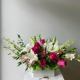 Pink roses and white lilies arranged in a white box
