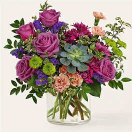 Purple roses and mixed flowers arranged in a clear glass vase with a succulent center.