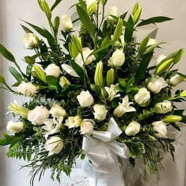 Large white lily and rose arrangement in a white vase with ribbon