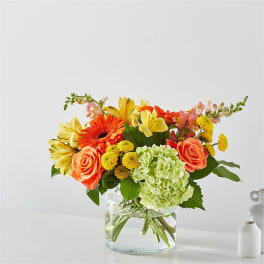 Mixed bouquet of orange roses, yellow lilies, and green hydrangea in a glass vase