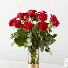 Red roses arranged in a clear glass vase with a gold base