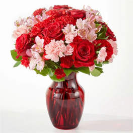 Red roses and pink flowers arranged in a red glass vase