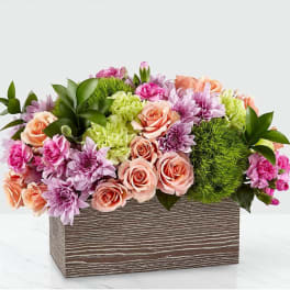 Mixed pink, peach, and lavender flowers arranged in a rectangular wooden box