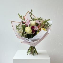 Hand-tied bouquet of pastel flowers wrapped in white paper