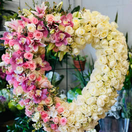 Heart-shaped floral arrangement of pink and cream roses with orchids