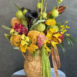 Mixed tropical bouquet in a speckled ceramic vase with bright yellow and pink blooms