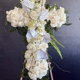 White floral cross arrangement on an easel with roses and orchids