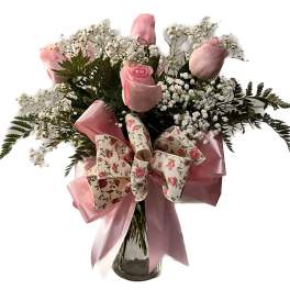 Pink roses in a glass vase with baby's breath and a floral bow