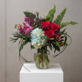 Mixed bouquet of red roses, blue hydrangea, and pink flowers in a glass vase