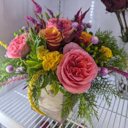 Colorful arrangement of pink and orange roses with yellow blossoms in a wooden cube vase