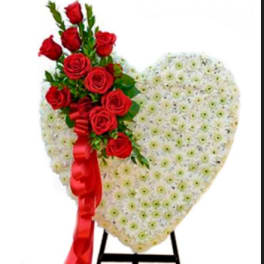 Heart-shaped floral tribute with red roses and a red ribbon on a stand