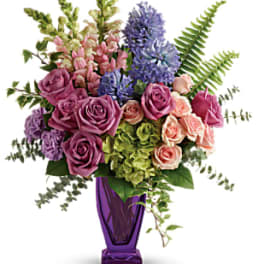 Mixed bouquet of roses, snapdragons, and purple blooms in a purple vase