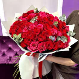 Large hand-tied bouquet of red and hot pink roses wrapped in white paper with a red ribbon.