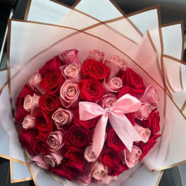 Bouquet of red and pink roses wrapped in white paper with a pink bow