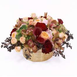 Low arrangement of red and peach roses, dark calla lilies, and orchids in a round gold vase