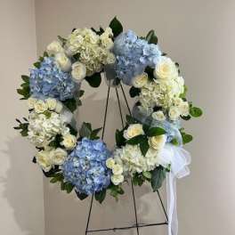 Blue and white floral wreath on a stand with a white ribbon