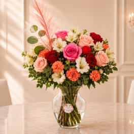Mixed bouquet of pink, red, peach, and white flowers in a clear glass vase