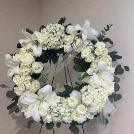 White floral wreath on a stand with lilies and roses