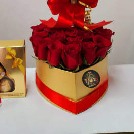 Red roses in a gold heart-shaped box beside a boxed chocolate gift