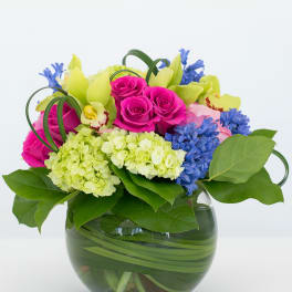 Bright mixed bouquet in a glass vase with pink roses and blue flowers