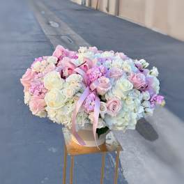 Large pastel bouquet of roses and hydrangeas in a white container with a pink ribbon