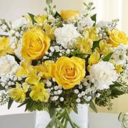 Yellow roses and white flowers arranged in a clear glass vase