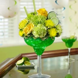 Yellow flowers arranged in a green margarita glass with lime slices