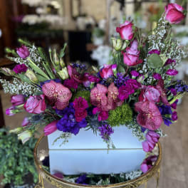 Mixed pink and purple floral arrangement in a white box