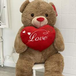 Large teddy bear holding a red heart pillow with the word Love