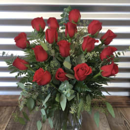 Red roses arranged in a clear glass vase with greenery