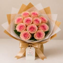 Bouquet of pink roses wrapped in white and gold paper with a satin ribbon