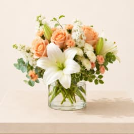 Peach roses and white lilies arranged in a clear glass vase