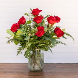 Red roses arranged in a glass vase with mixed greenery