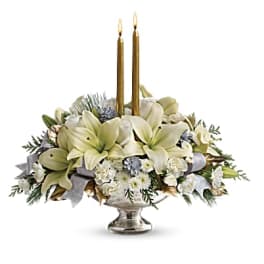 White floral centerpiece with two gold taper candles in a silver vase