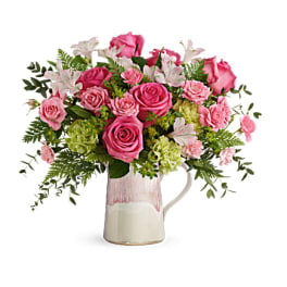Pink roses and lilies arranged in a ceramic pitcher vase