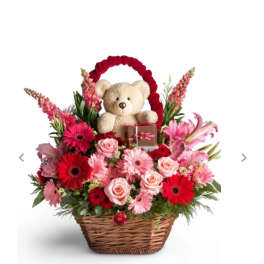 Basket arrangement with pink and red flowers, a teddy bear, and a small gift box