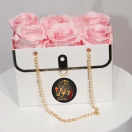 Pink roses arranged in a white gift box with a gold chain strap.