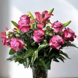 Pink roses and a lily arranged in a clear glass vase