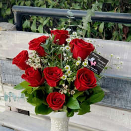 Red roses arranged in a white vase with small white filler flowers.