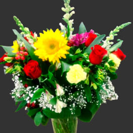 Mixed bouquet of red roses, yellow sunflower, and pink flowers in a glass vase
