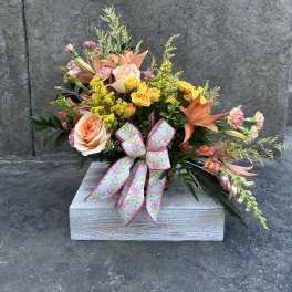 Mixed bouquet of peach roses, yellow spray roses, and orange lilies in a wooden box