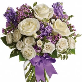 White roses and purple flowers in a glass vase with a purple ribbon